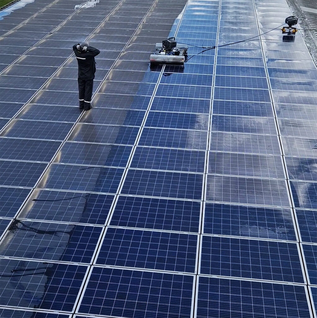 Solarreinigung in Aktion: Person steht auf Dach und bedient einen Roboter für Solarreinigung. Man sieht auf der einen Seite gereinigte, saubere Solarmodule und auf der anderen Seite schmutzige , die noch eine Solarreinigung brauchen. Ausgeführt von SoluShine Solarreinigung.